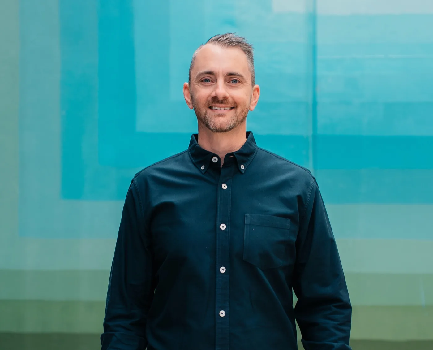 James Richardson in a navy shirt, smiling, in front of a teal wall