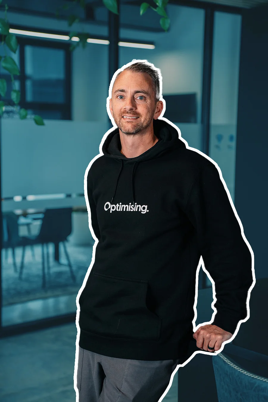 James in a black Optimising hoodie, leaning on a chair in the office