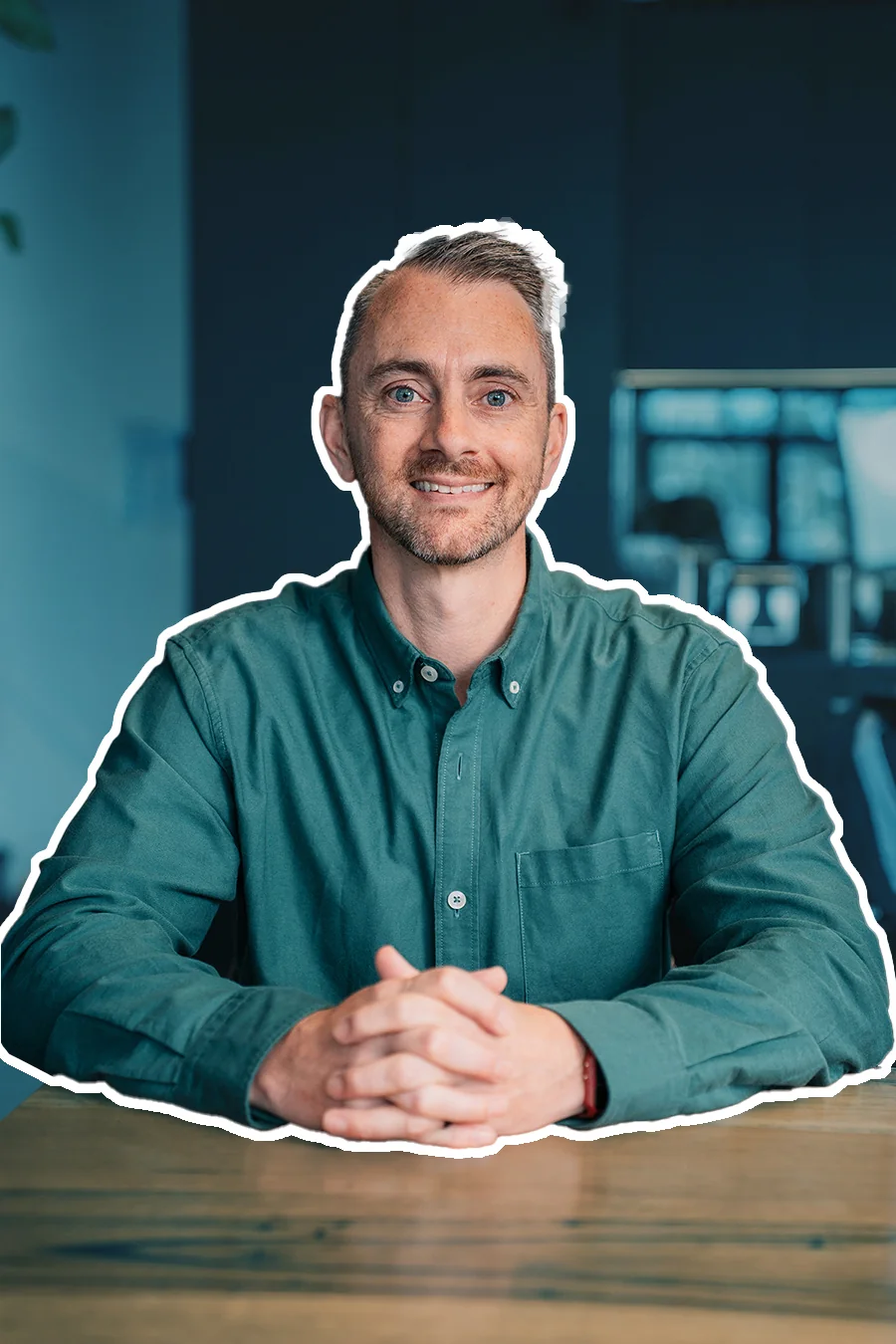 James in a green shirt at a desk, hands clasped, smiling