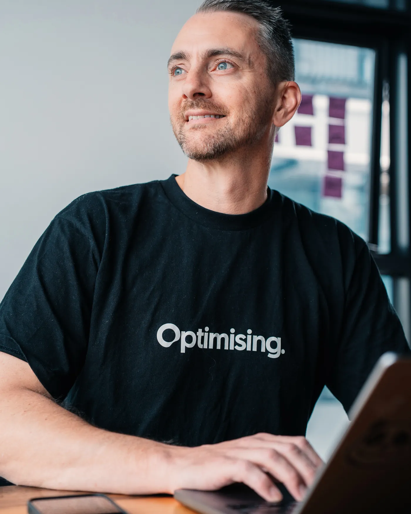 James at his laptop in an Optimising t-shirt, looking out the window